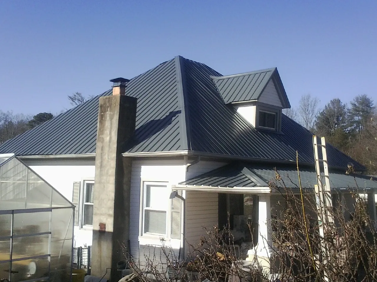 Dark blue standing seam metal roof on a white farmhouse with dormer — Slate & Tile Roof Repair by Roofing Brothers in Harper Woods