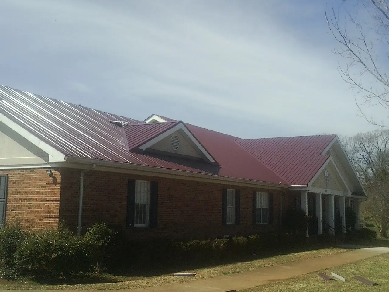 Red metal roof with gabled entries on a long brick building, from a Hail Damage Roof Repair job in Harper Woods