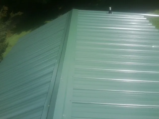 New green metal panels meeting at the ridge of a roof — Flat Roof Repair work by our crew in Harper Woods