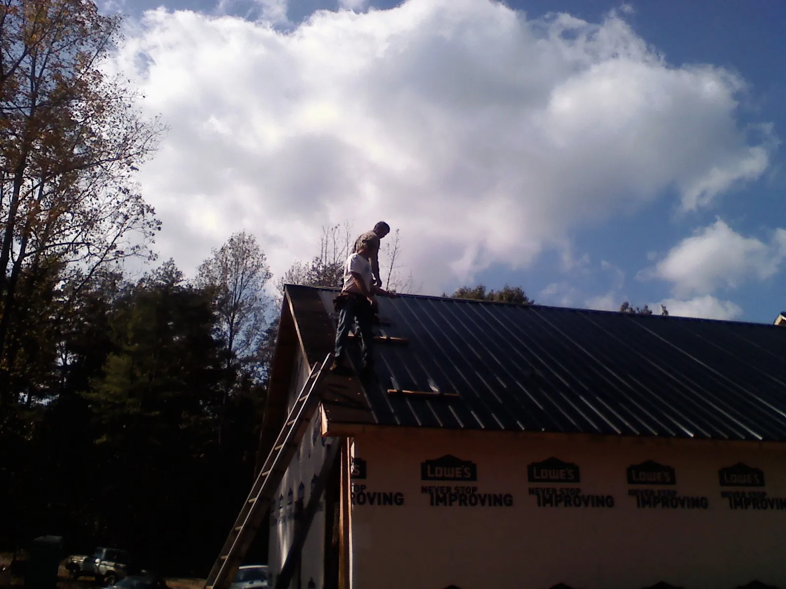 Roofer fastening dark metal panels high against a cloudy sky, from a Roof Inspection job in Harper Woods