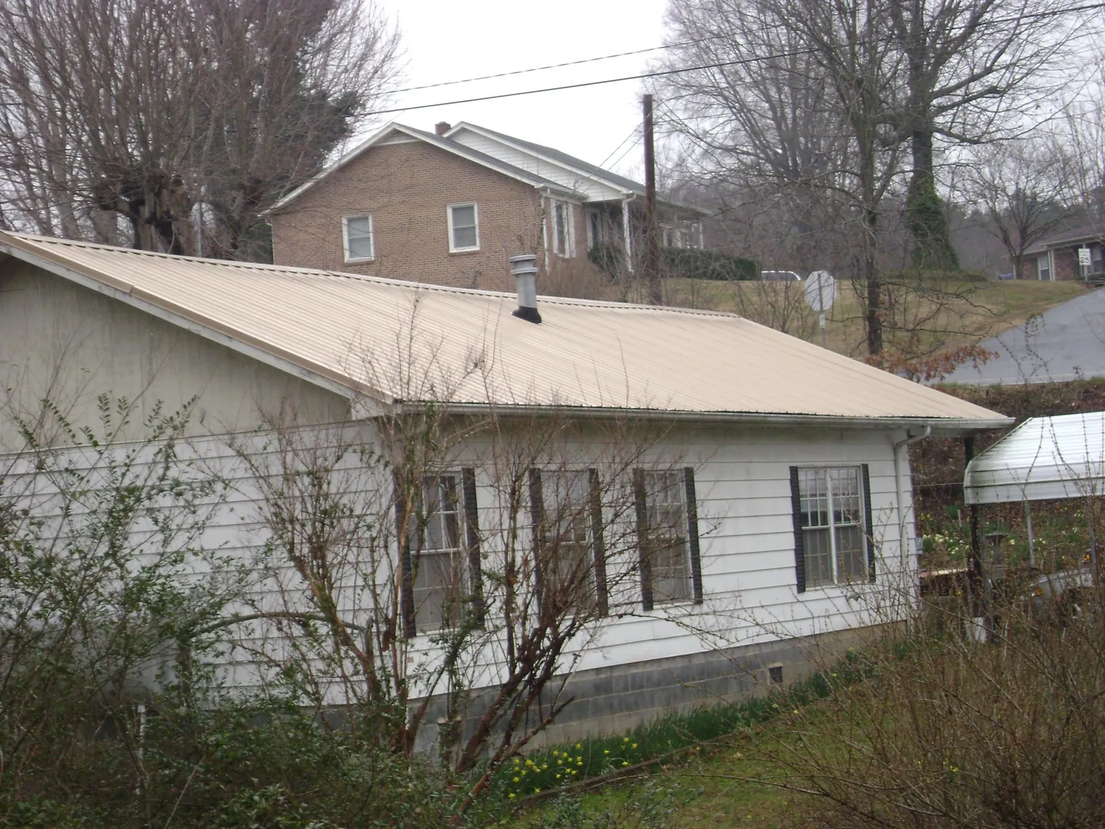 Tan metal roof on a white sided house set into a hillside — Commercial Roofing by Roofing Brothers in Harper Woods