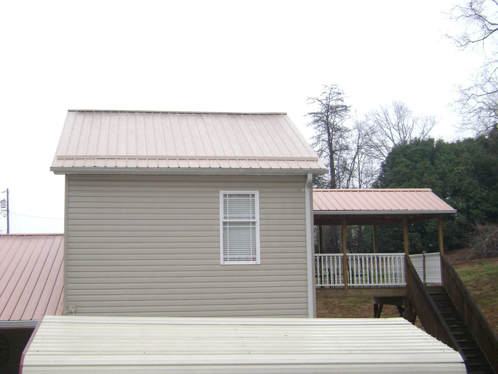 Tan metal roofs on a two story addition and attached porch, from a Roof Replacement job in Harper Woods